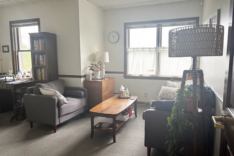 A cozy counseling room with seating, a bookshelf, and natural light